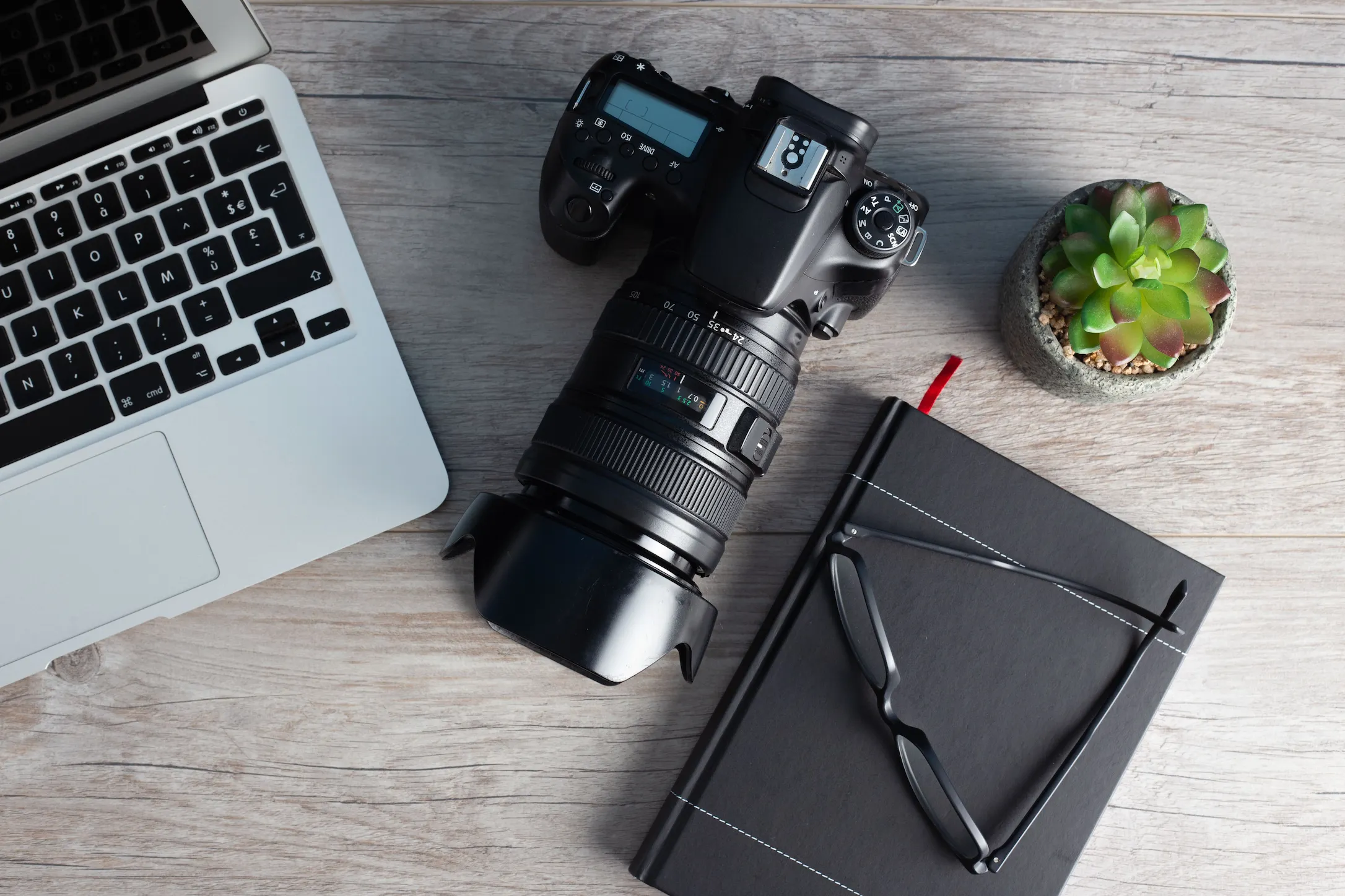 Flat lay of content creation tools including a camera, laptop, notebook, and glasses on a desk