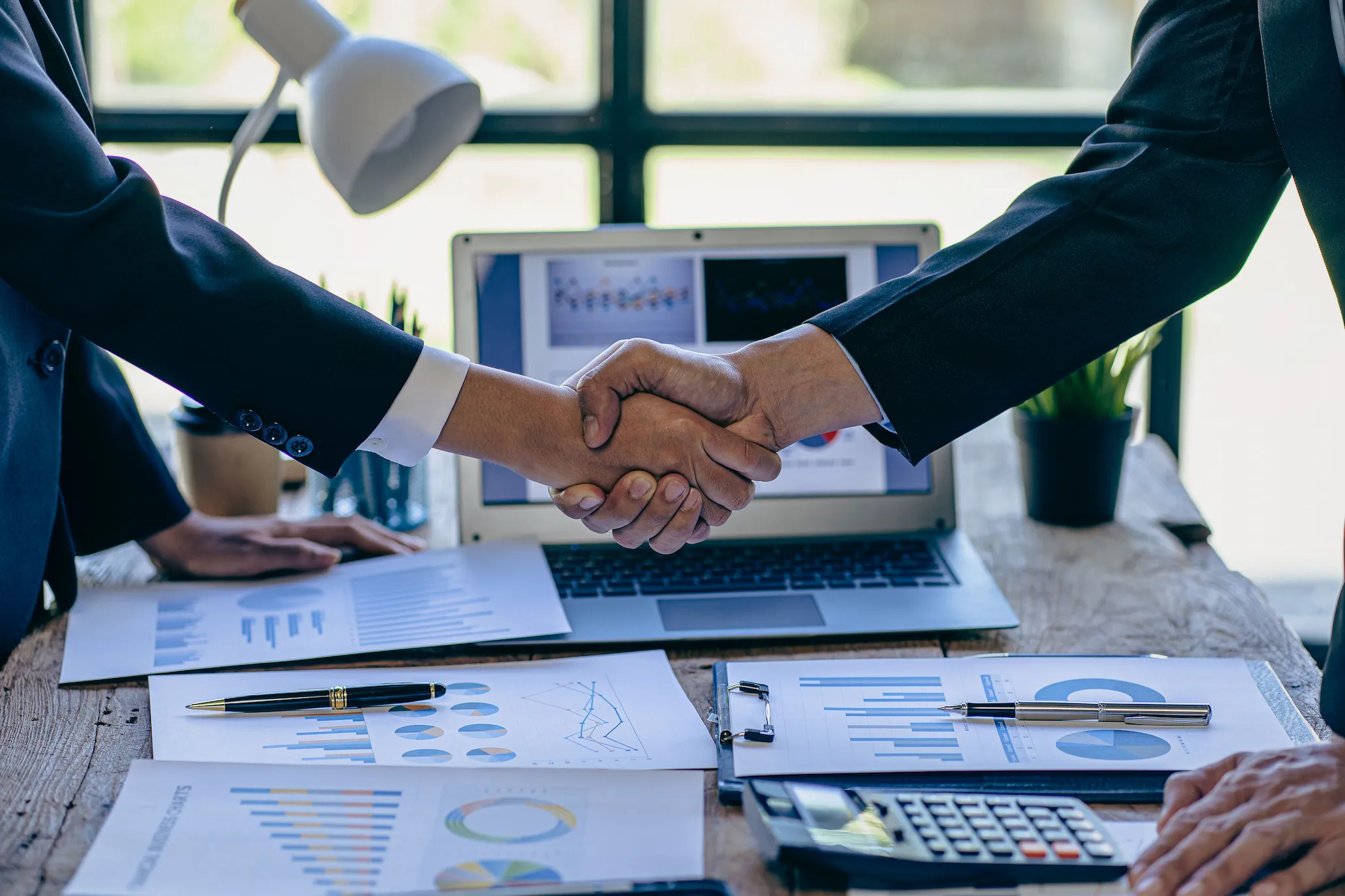 Business professionals shaking hands over PPC advertising charts and campaign data