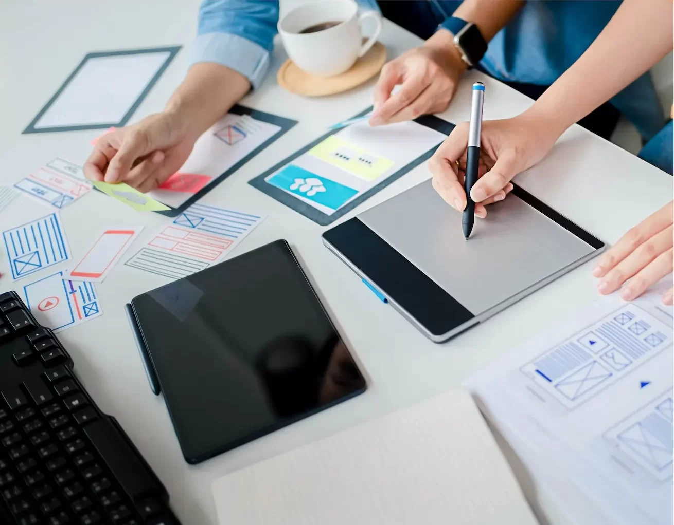Hands collaborating on digital content planning with tablets and wireframes on a modern workspace for Unclaimed social media management services.