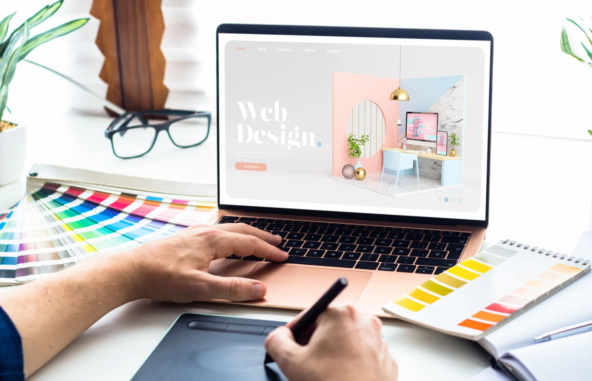 Person working on web design using a graphic tablet and color swatches beside a laptop displaying a design project.